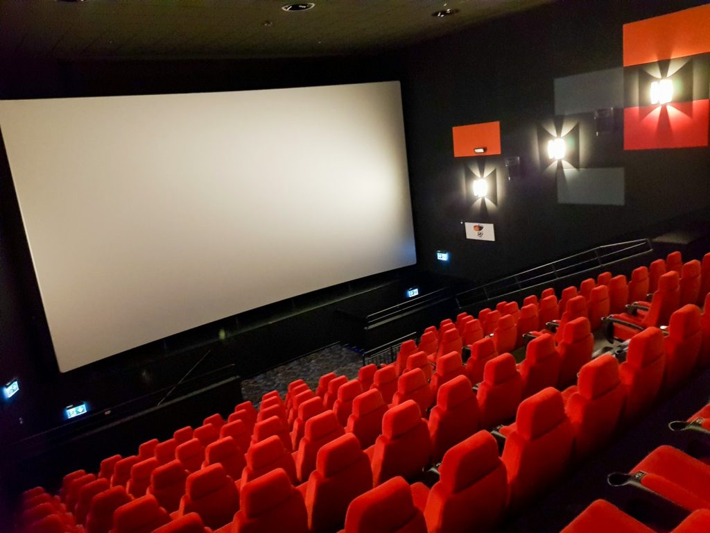 an empty theater with red seats and a projector screen